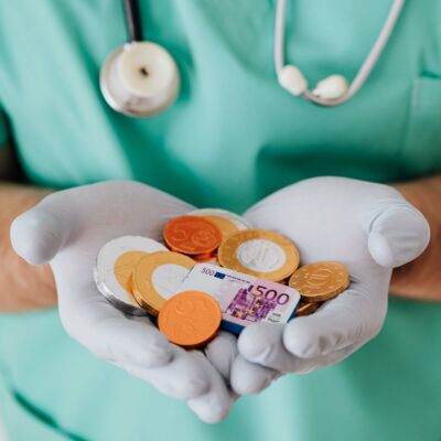 Arzt / Ärztin hält Münzen und Geldscheine in der ausgestreckten Hand